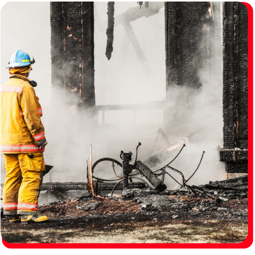 A firefighter stands in front of a smoke-filled, severely burned and collapsed structure, indicating the aftermath of a large-scale fire loss in Toronto, Ontario, Canada.
